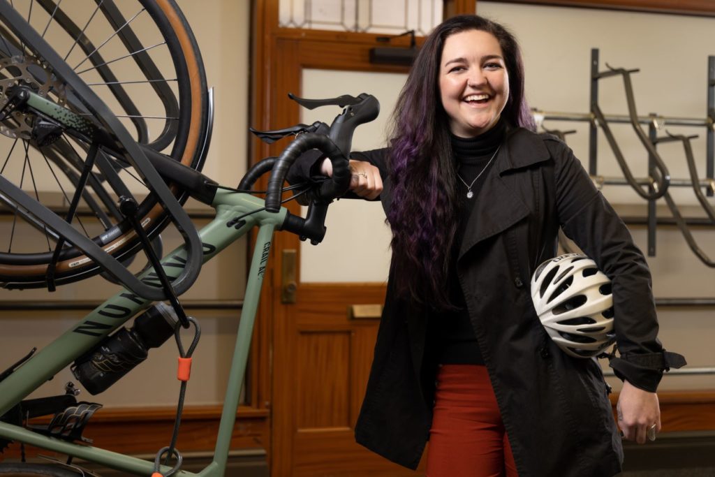 woman smiling next to bike, holding helmet
