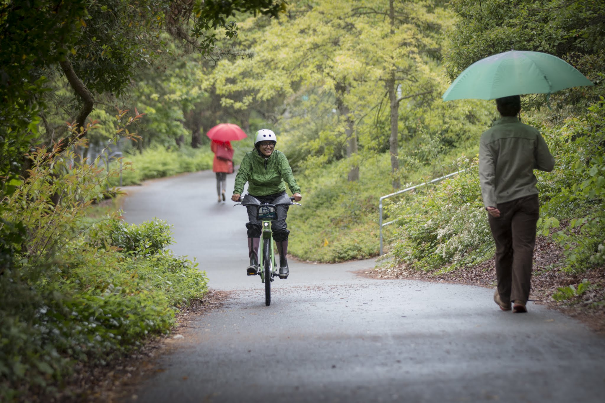 A cyclist in rain gear and a helmet rides past umbrella-toting pedestrians